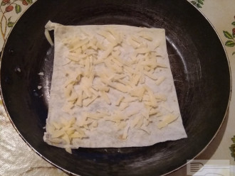 Шаг 2: Лаваш разрежьте на два квадратных кусочка. Один положите на сковородку и насыпьте на него часть сыра.