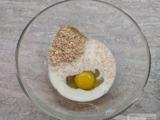 Шаг 2: В большую миску разбейте яйцо, добавьте небольшую щепотку соли, овсяные хопья и молоко.