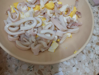 Шаг 3: Снимите пленочку с тушки кальмара. Нарежьте кальмара полукольцами и добавьте к яйцам.