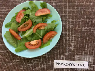 Шаг 2: Порвите салат руками и выложите на тарелку. Нарежьте помидор дольками и выложите на листья салата.