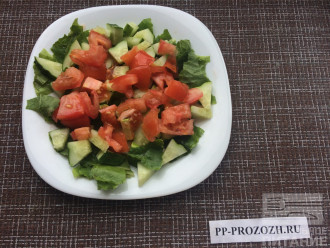 Шаг 2: Порвите руками листья салата и выложите на тарелку. Крупно нарежьте помидор и огурец. Выложите поверх листьев салата.
