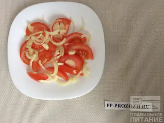 Шаг 2: Нарежьте помидор крупными ломтиками, выложите на тарелку. Лук порежьте полукольцами, выложите поверх помидора.