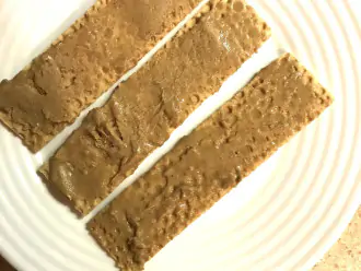 Шаг 2: Намажьте хлебцы тонким слоем арахисовой пасты. 