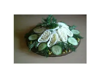 Шаг 7: Выложите готовый салат горкой на блюдо, украсьте колечками кальмаров, ломтиками огурцов, желтками яиц и зеленью.