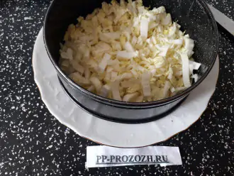 Шаг 3: Возьмите тарелку и положите на неё разъёмную форму. Выложите первым слоем пекинскую капусту. Посолите, поперчите, сбрызните растительным маслом.