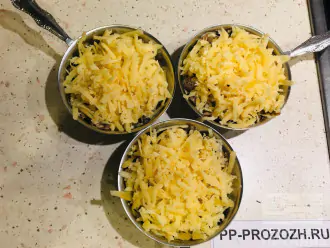 Шаг 7: Выложите обжаренные лук, грибы и сметану в кокотницы, посыпьте натертым на тёрке сыром и поставьте в разогретую до 200 градусов духовку на 10-15 минут.