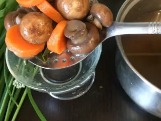 Шаг 4: После того, как грибы и морковь сварились, аккуратно достаньте грибы и морковь из бульона шумовкой в неглубокую тарелку. Грибной бульон необходимо охладить. 