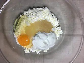 Шаг 2: В глубокую миску положите творог, разбейте яйцо, добавьте мёд и сметану.
