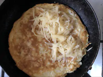 Шаг 5: Блин переверните, на половину положите тертый сыр, накройте второй половиной и закройте сковороду крышкой.